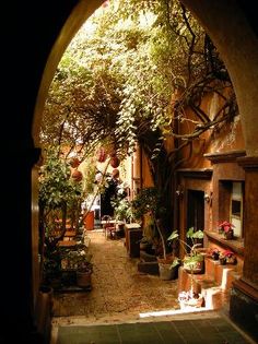 an archway leading into a courtyard with potted plants on either side and pots in the middle