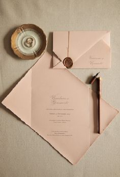 the wedding stationery is laid out on top of an envelope, with a pen and inkwell