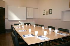 a long table with coffee cups on it in a room that has white walls and wooden floors