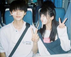 two people sitting on a bus with their fingers in the air and one person holding up peace signs