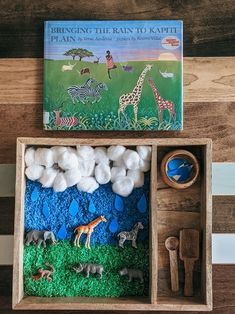 a wooden box filled with toys and books on top of a wood table covered in grass