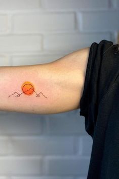 a woman's arm with a small orange ball tattoo on the left inner arm