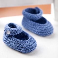 two crocheted blue baby shoes sitting on top of a white table next to a rocking chair