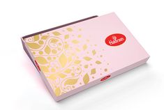 a pink box with gold designs on the front and sides, sitting on a white surface