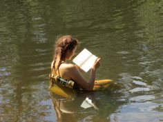 a woman sitting in the water reading a book