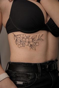 a woman's stomach with flowers and leaves on her side, showing the tattoo