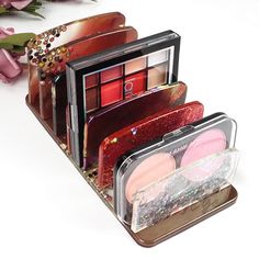 three different types of makeup in a tin with flowers on the table next to it