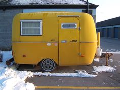 a small yellow trailer parked in front of a building with snow on the ground and around it