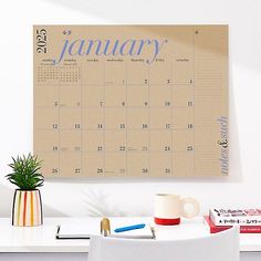 a desk with a calendar on the wall next to a coffee cup and pen holder