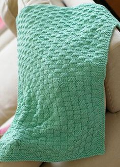 a green knitted blanket sitting on top of a couch next to a white chair