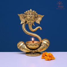 an ornate brass ganeshi lamp on a white table with orange flowers and blue background