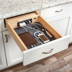 an open drawer in the middle of a kitchen with electronic devices and cords on it