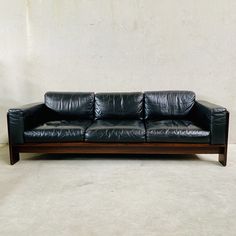 a black leather couch sitting on top of a white floor next to a wooden frame