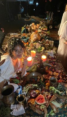 two women sitting at a long table with food and candles in front of them, surrounded by other people