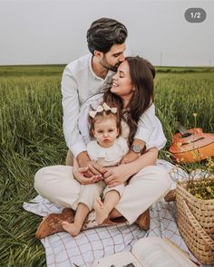 a man, woman and child sitting on a blanket in a field with an open book