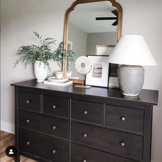 a dresser with a mirror, lamp and pictures on it