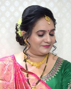 a woman in a green and pink sari with gold jewelry on her neck, looking down