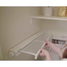 a woman is opening the door to an empty cabinet in her kitchen, while she's working on something