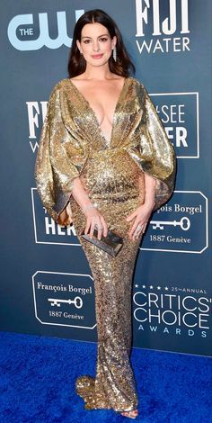 a woman in a gold dress standing on a blue carpet with her hand on her hip