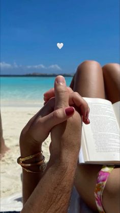 a person sitting on the beach reading a book with a white heart floating above them