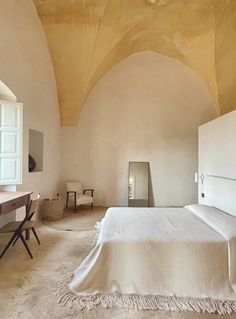 a bedroom with a bed, desk and mirror on the wall next to an arched ceiling