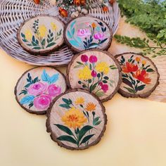 painted wooden slices with flowers on them sitting on a table next to plants and baskets