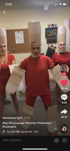 three people wearing paper hats and red shirts are standing in a room with cardboard boxes on their heads