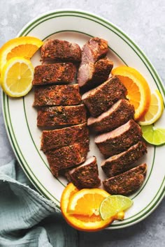 slices of meat on a plate with oranges, limes and lemon wedges