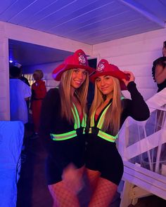 two women dressed in costumes posing for the camera with one woman wearing a red fireman's hat