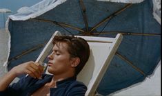 a man laying on top of a beach chair next to an umbrella and holding a drink