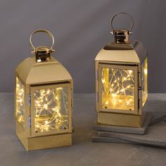 two gold lanterns with lights on them are sitting on a gray surface and one is lit up