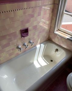 a bath tub sitting next to a toilet in a bathroom with pink tiles on the walls