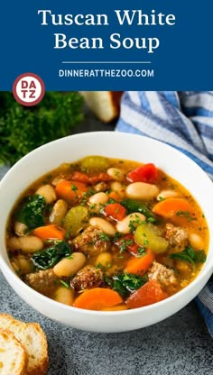 a white bowl filled with bean and vegetable soup next to some bread on the side