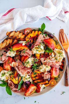 a white plate topped with grilled peaches and other food next to utensils