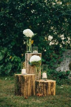 three vases with white flowers and candles are sitting on wooden stumps in the grass