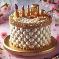 a white cake with gold decorations and lipsticks on it's top, surrounded by pink flowers