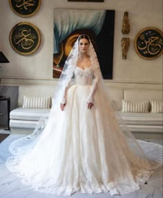 a woman in a white wedding gown and veil standing on a bed with an ornately decorated wall behind her