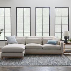 a living room with large windows and a sectional couch in front of a blue rug