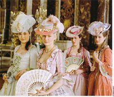 three women in period dresses and hats holding fans