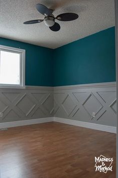 empty room with blue walls and wood flooring, ceiling fan in the corner between two windows