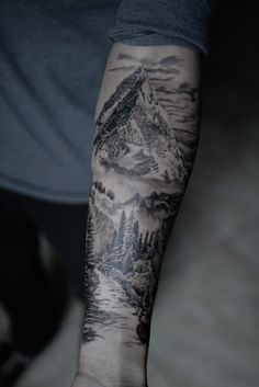 a man's arm with a mountain scene on it and trees in the background