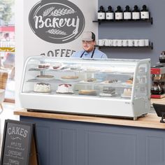 a man standing behind a bakery counter filled with cakes