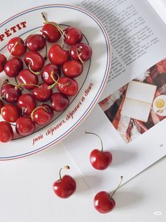 some cherries are sitting on a plate next to an open book