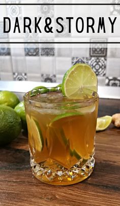 a glass filled with liquid and limes on top of a wooden table