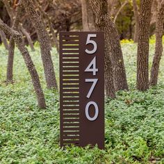 a sign that is in the grass near some trees and bushes with numbers on it