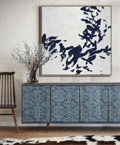 a painting hangs on the wall next to a blue and white cabinet with flowers in it