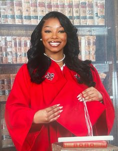 a woman in a red graduation gown is holding a book and smiling at the camera