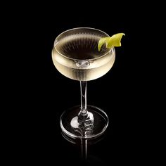 a drink with a lime garnish sitting in a wine glass on a black background