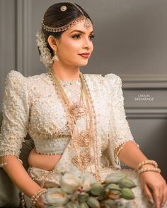 a woman in a white dress sitting on a chair with flowers and pearls around her neck