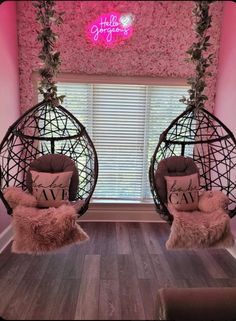 two hammock chairs in front of a window with pink flowers on the wall